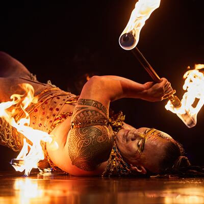 Un cracheur de feu qui danse couché sur le sol tient des bâtons enflammés dans les airs - Spectacle Cirque du Soleil