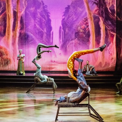 Two acrobats lying on their backs, juggling with their feet, gracefully tossing and catching their partners.