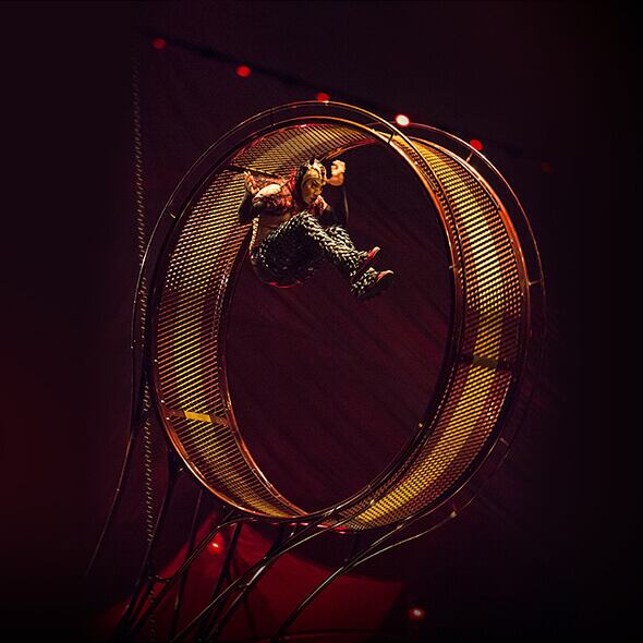 El artista se cuelga en un artilugio giratorio metálico redondo llamado Rueda de la Muerte - Kooza Cirque du Soleil