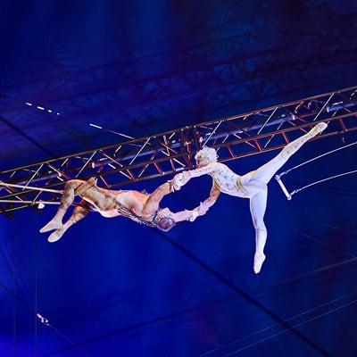 An upside down trapezist grabs a flyer during a high-flying finale - Cirque du Soleil Alegría