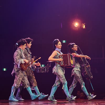 Four musicians walking while playing brass, string, and accordion - circus Alegría