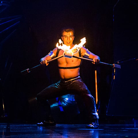A fire dancer holds two flaming sticks on stage - Bazzar Cirque du Soleil