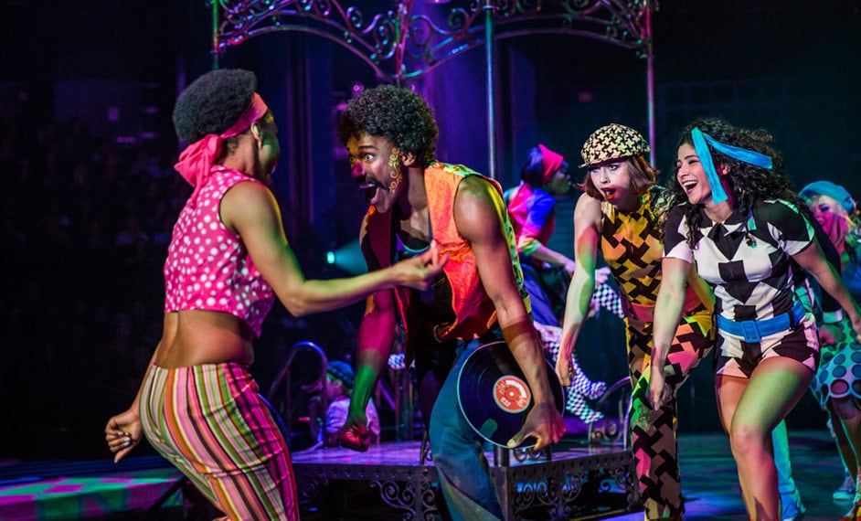 Personajes vestidos con ropas de colores bailan sobre el escenario al ritmo de los años 60 - The Beatles Love Cirque du Soleil