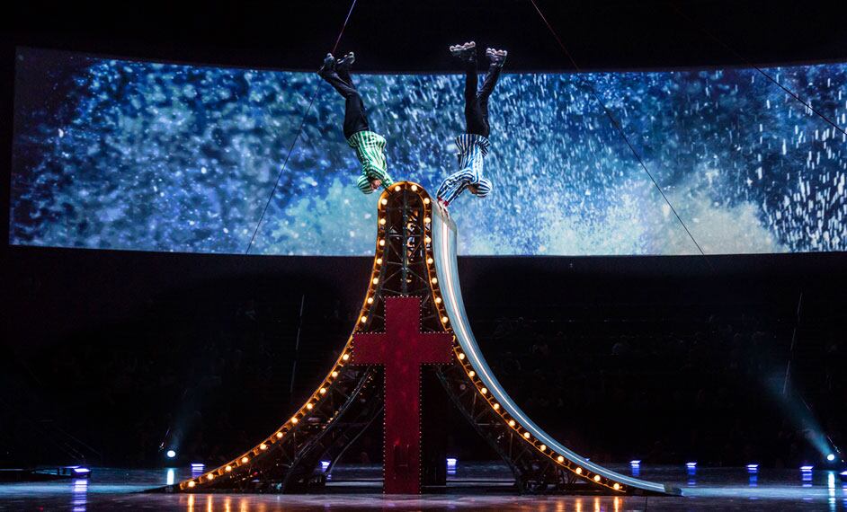 Dos patinadores acrobáticos sostienen boca abajo hasta el extremo superior de una pista de patinaje - The Beatles Love Cirque du Soleil