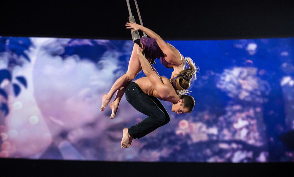 Dos trapecistas se aferran a un columpio alto sobre el escenario - The Beatles Love Cirque du Soleil