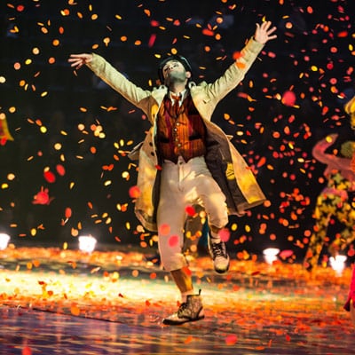 An artist dances dressed in a beige overcoat while confetti rains over the stage - The Beatles Love Las Vegas