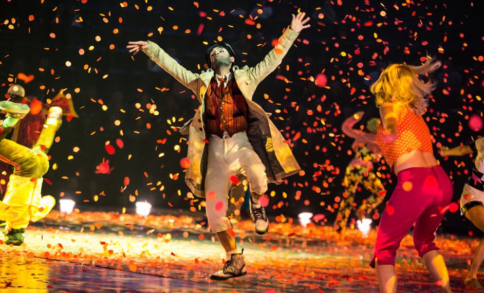 Un artista baila vestido con un abrigo beige mientras el confeti llueve sobre el escenario - The Beatles Love Cirque du Soleil