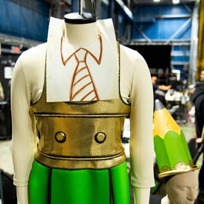 Un mannequin en forme de crayon porte une cravate dessinée sur le cou, un chemisier doré et un pantalon vert - Cirque du Soleil Orlando
