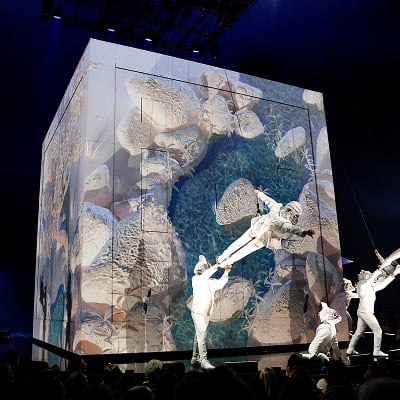 Acróbatas vestidos de animales cuelgan en posición vertical en el CUBO, una arquitectura en el escenario de ECHO. 