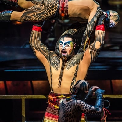 Muscled and tattooed man carries an enemy over his head in a battle choreography - Cirque du Soleil Kà