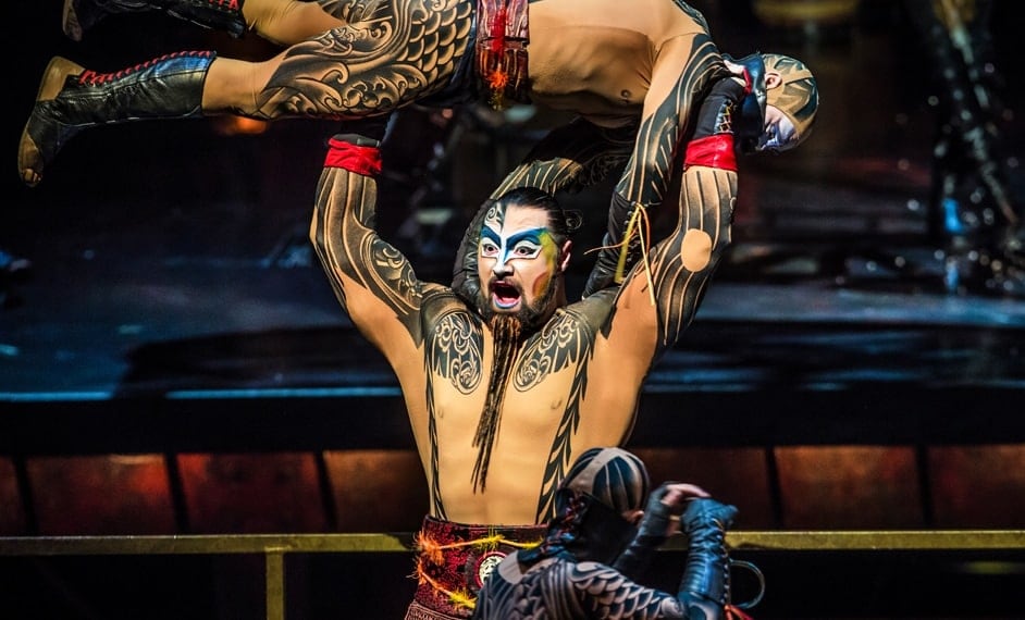 Muscled and tattooed man carries an enemy over his head in a battle choreography - Cirque du Soleil Kà