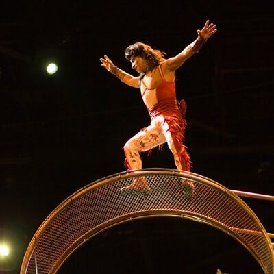 Un hombre vestido con un traje blanco y rojo se balancea sobre la rueda del artilugio de la muerte - Kà Cirque du Soleil
