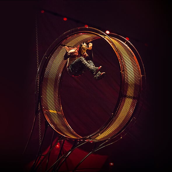 El artista se cuelga en un artilugio giratorio metálico redondo llamado Rueda de la Muerte - Kooza Cirque du Soleil