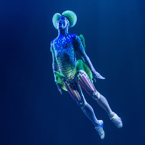 Une créature sous-marine à l'aspect humain rebondit dans les airs pendant le numéro de trampoline - Kurios Cirque du Soleil