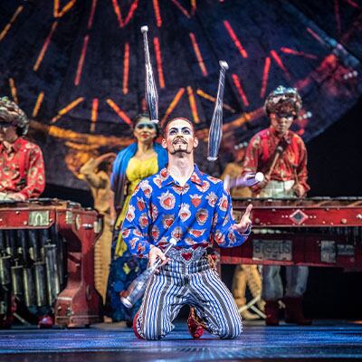 Un artiste de cirque jongle avec des quilles pendant que des musiciens jouent en arrière-plan - durée du spectacle Luzia