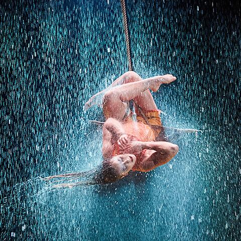 A trapeze artist twirls under pouring rain in the show LUZIA