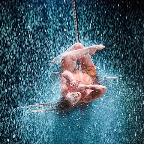 A trapeze artist twirls under pouring rain in the show LUZIA