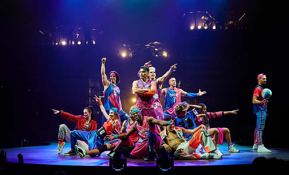Bailarines vestidos con ropa de baloncesto posan en el escenario y miran a la multitud - Mad Apple Cirque du Soleil