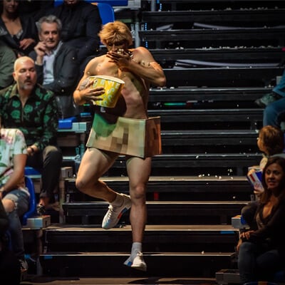 A streaker eating popcorn while descending amphitheater stairs catches the attention of every spectator - Cirque du Soleil Messi