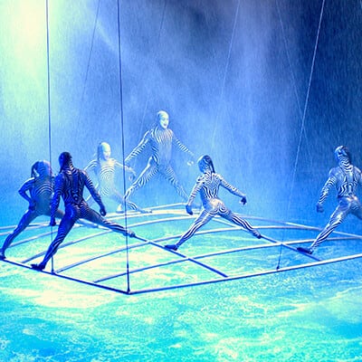 Artists dressed in zebra striped clothing dance on a metallic frame over water - Cirque du Soleil O