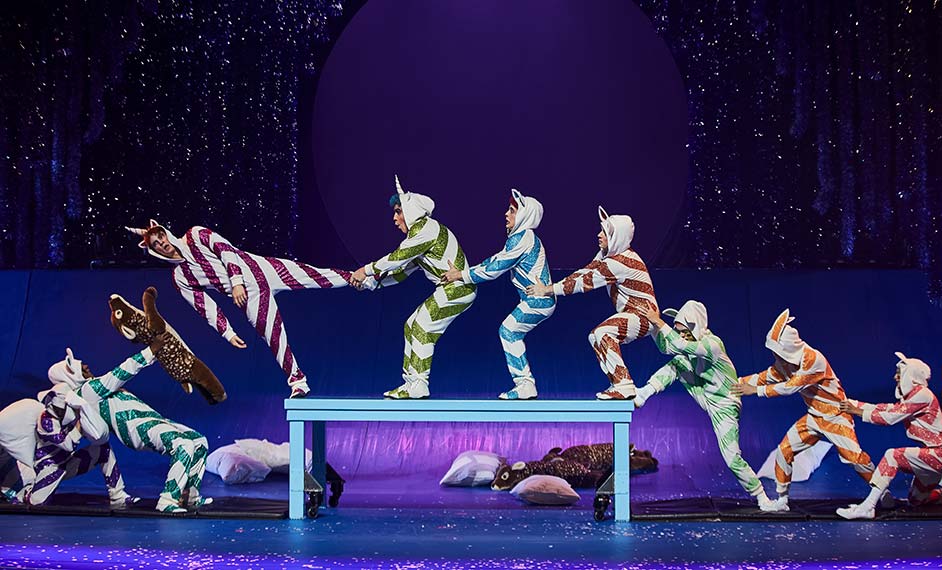 Group of children in colorful pajamas perform acrobatics on an acro table - Cirque du Soleil Christmas