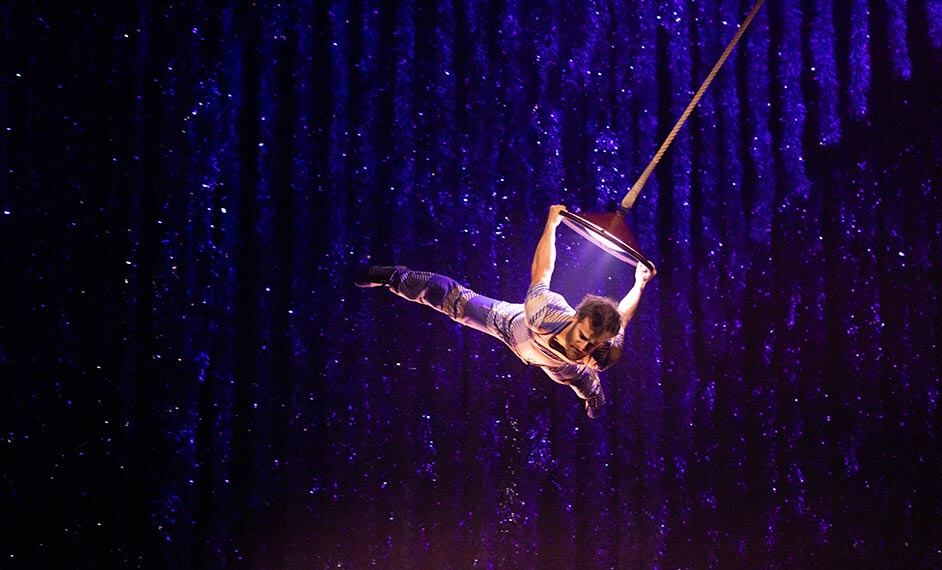 Gymnast performs an aerial act holding onto a balancing lamp in the air - Christmas Cirque du Soleil