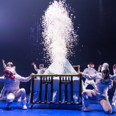 Six mischievous elves dressed in white clothing dance around a bed - Cirque du Soleil Twas The Night Before show