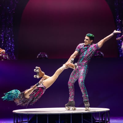Two artists perform a roller skate duo on a small and round white platform - Twas The Night Before cirque Christmas show